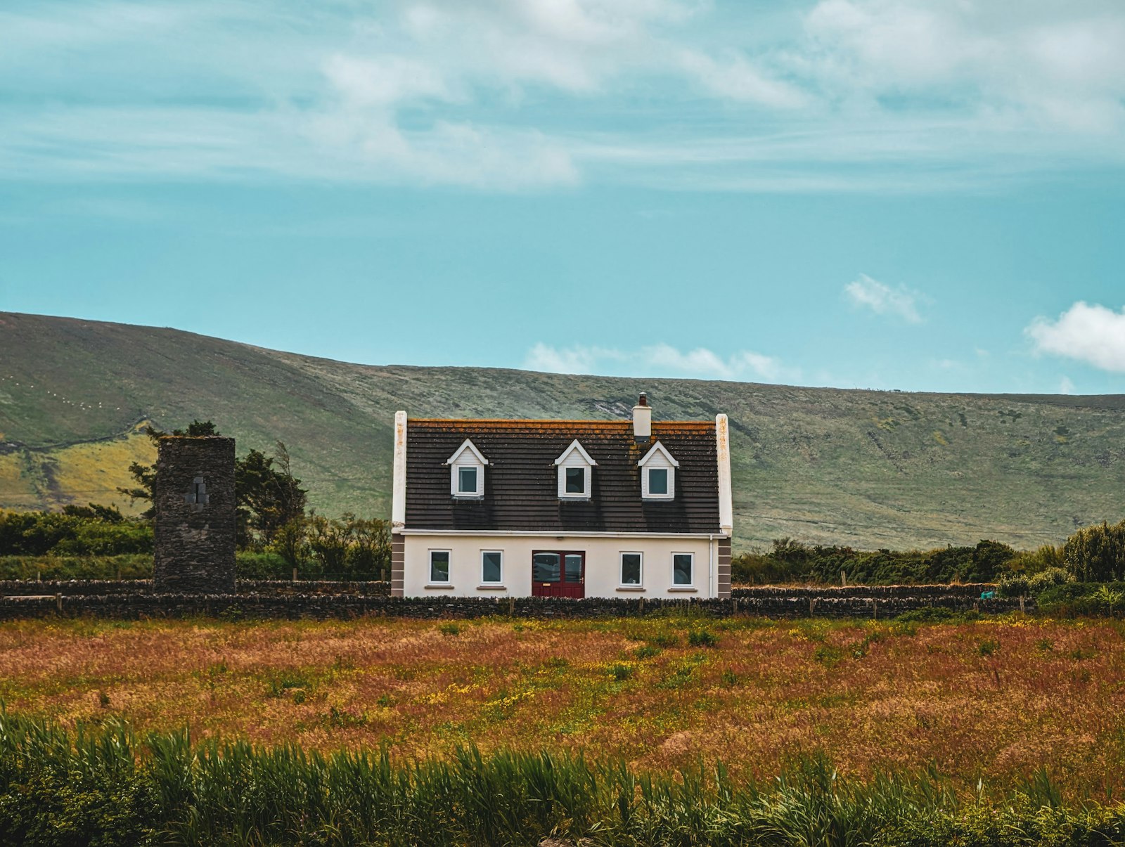 A modern detached two-storey Irish home with white walls and dormer windows, set against the Kerry mountains